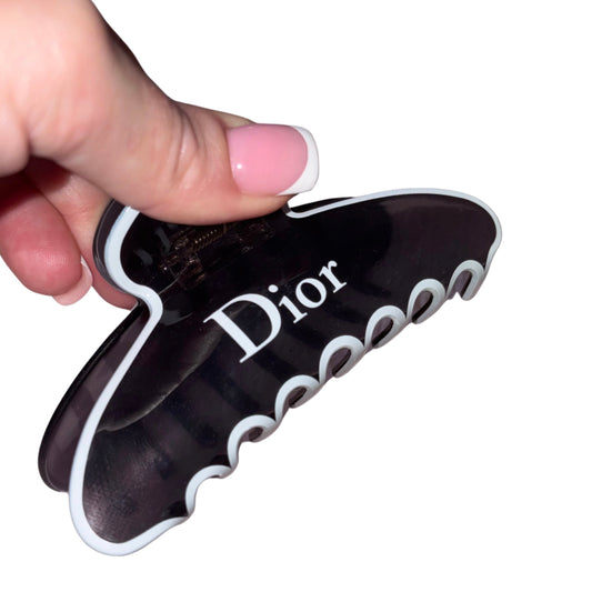 Close-up of a hand with a pink French manicure holding a high-gloss black and white designer text claw clip hair accessory.