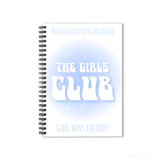 A white spiral-bound notebook with a black wire binding, featuring the text 'MANIFESTATION JOURNAL', 'THE GIRLS CLUB', and 'GIRL BOSS EDITION' in white and light blue on the cover by Gypsy Soul Doll.