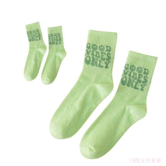 Pair of aesthetic vibrant green crew socks featuring a retro wavy dark green text print that reads Good Vibes Only with smiley faces.