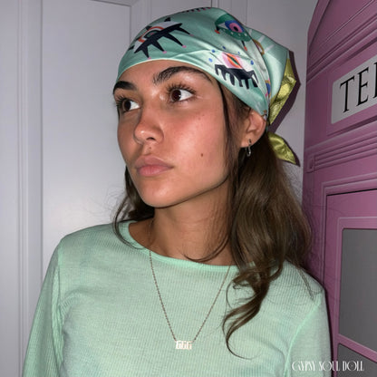 A model wearing a green evil eye silk boho headscarf paired with a matching mint green ribbed long-sleeve top and an Angel number 666 gold necklace.