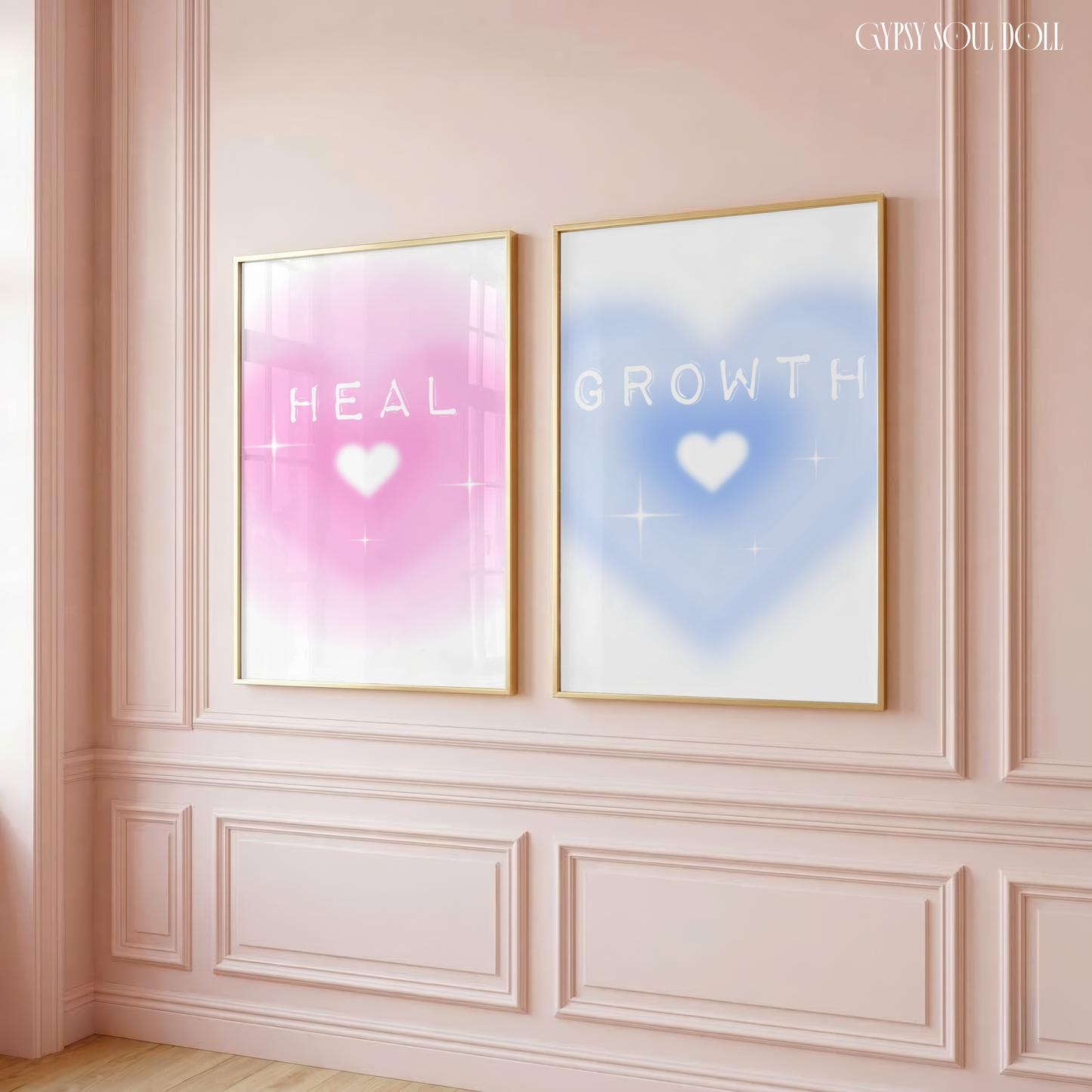 Two gold-framed spiritual wall prints hanging on a dusty pink panelled wall, featuring a pink gradient aura print reading HEAL and a blue gradient aura print reading GROWTH with white hearts.