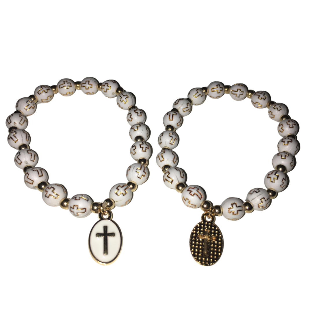 Two Gypsy Soul Doll Holy Devotion stretch beaded bracelets displayed side by side against a white background, featuring white round beads with gold cross engravings, one showcasing a white enamel oval cross charm and the other a textured gold mesh cross pendant.