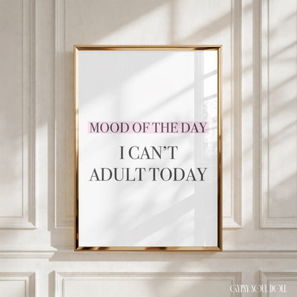 A framed typographic wall art print hangs on a white paneled wall. The print has a thin gold frame and reads “MOOD OF THE DAY I CAN’T ADULT TODAY,” with “MOOD OF THE DAY” highlighted in soft pink.