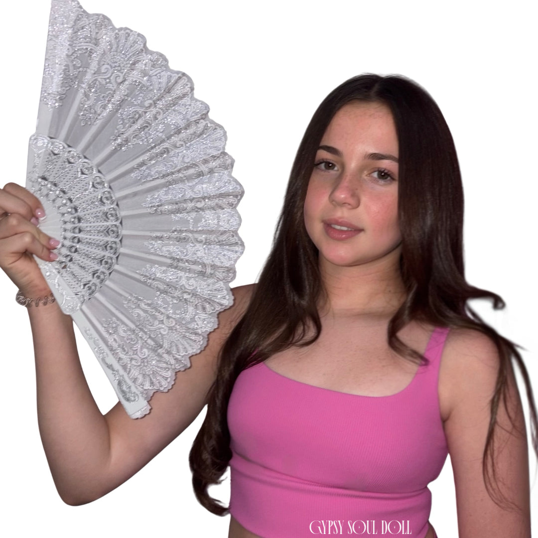 A young model with long dark brown hair holds up a white lace folding fan against a plain white background. She is wearing a bright pink tank top with the text 'GYPSY SOUL DOLL' printed on the front.