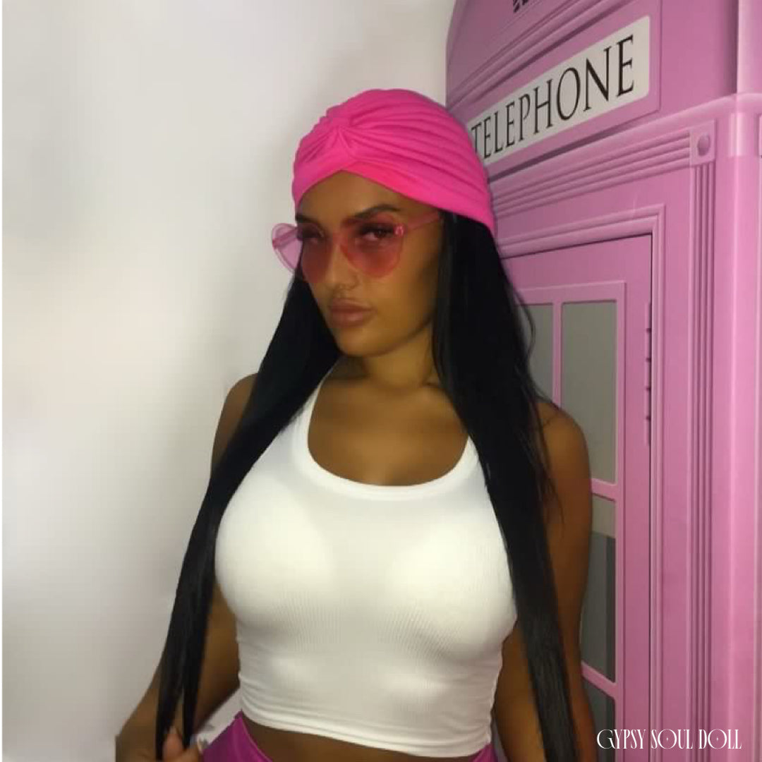 A woman wearing a bright pink headwrap, pink heart-shaped fashion glasses and a white ribbed crop top stands next to a pink telephone booth. The text 'GYPSY SOUL DOLL' is visible in the bottom right corner.