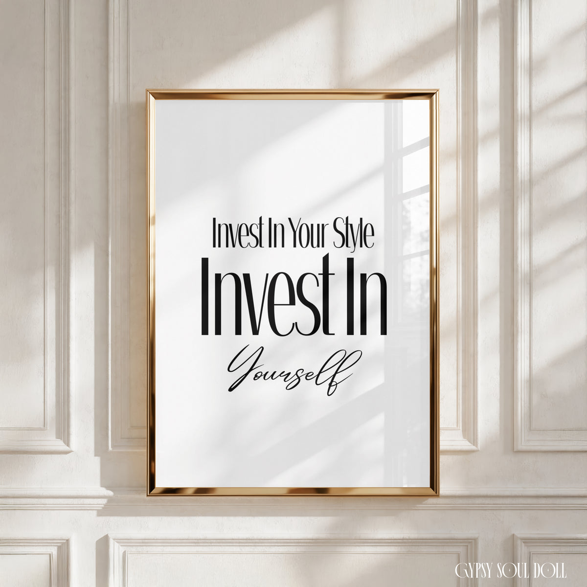 A framed motivational wall art print with the text 'Invest In Your Style Invest In Yourself' in black typography on a white background, enclosed in a thin gold frame and displayed against a white panelled wall with soft window shadows by Gypsy Soul Doll.