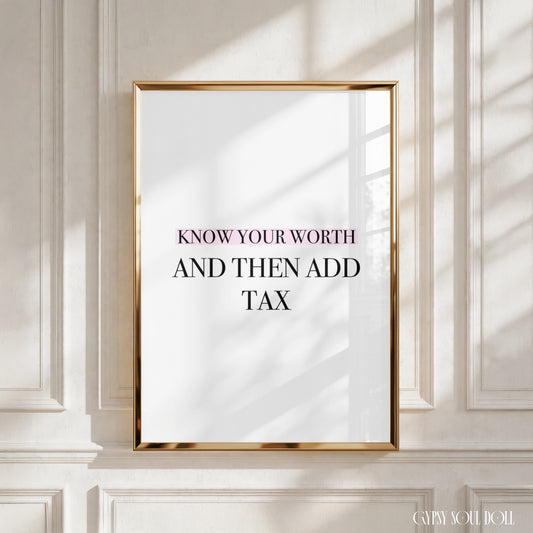 A framed art print with the text 'KNOW YOUR WORTH AND THEN ADD TAX' in black lettering on a white background, enclosed in a thin gold frame and leaning against a white paneled wall with soft window shadows.
