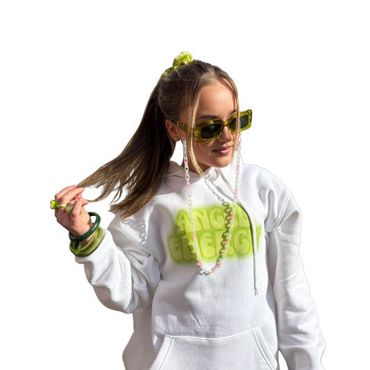 Front view of a model styling an oversized white hoodie with a vibrant lime-green Angel Energy front graphic, holding her ponytail, accessorised with a matching green scrunchie, green retro bracelets, chunky green girly rings, and matching fashion glasses.
