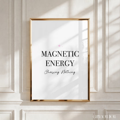 A framed wall art print with the text 'MAGNETIC ENERGY Chasing Nothing' in black lettering on a white background, enclosed in a thin gold frame and mounted on a white panelled wall with soft window shadows by Gypsy Soul Doll.