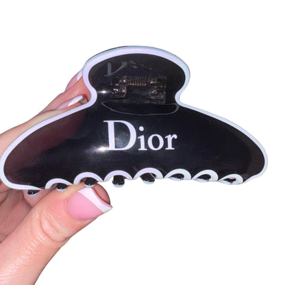 Close-up of a hand with a pink French manicure holding a high-gloss black and white designer text claw clip hair accessory.