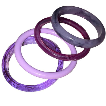 Four translucent bangles in shades of purple, lavender, and dark plum, arranged overlapping on a plain white backgroundby Gypsy Soul Doll.