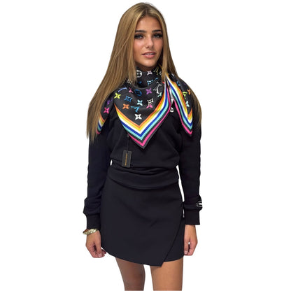 A woman modelling a black long-sleeve mini dress with a colourful striped and monogram patterned scarf, set against a plain white background.