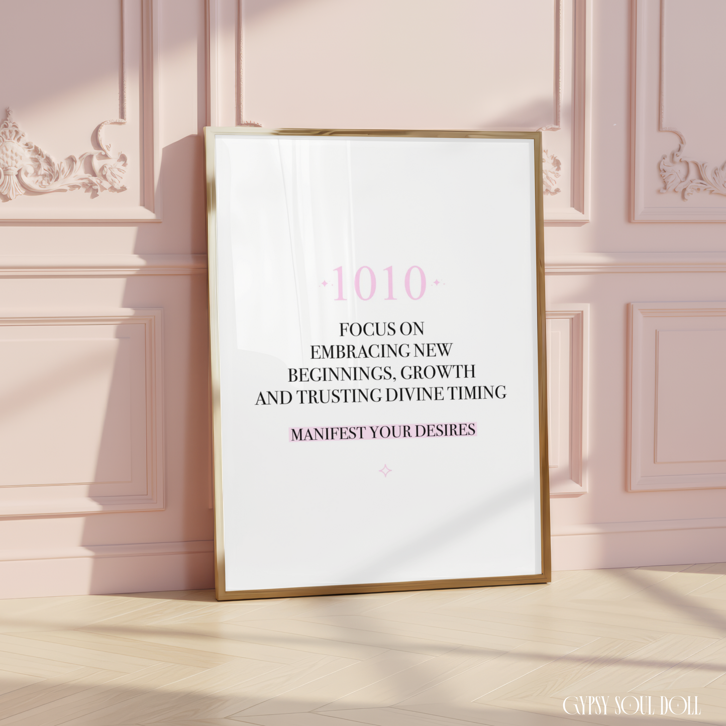 Minimalist A4 manifestation wall art print featuring the 1010 angel number in soft pink typography above a black text quote about embracing new beginnings, growth, and trusting divine timing, framed on a wooden floor against a pink panelled wall.