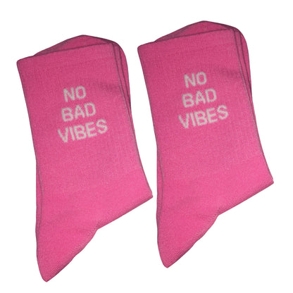 Two folded pink socks with the phrase 'NO BAD VIBES' printed in white on the front, displayed against a plain white background.
