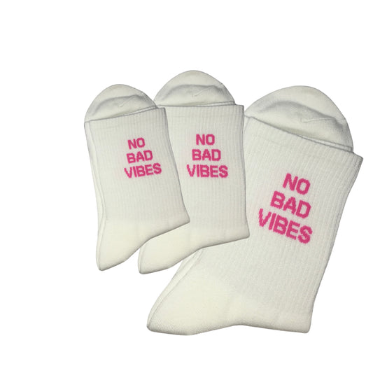 White crew socks with pink writing that reads ‘NO BAD VIBES’.