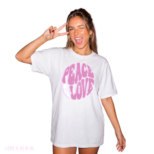 Model showcasing the Gypsy Soul Doll comfy 100% cotton white T Shirt featuring a round pink bubble typography design reading Peace and Love while flashing a peace sign.