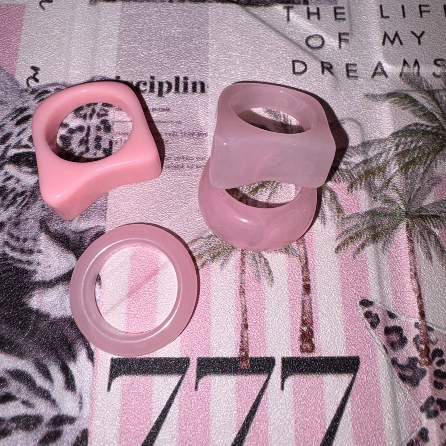 Four pink silicone rings displayed on a pink and white striped blanket with palm tree and leopard print patterns.