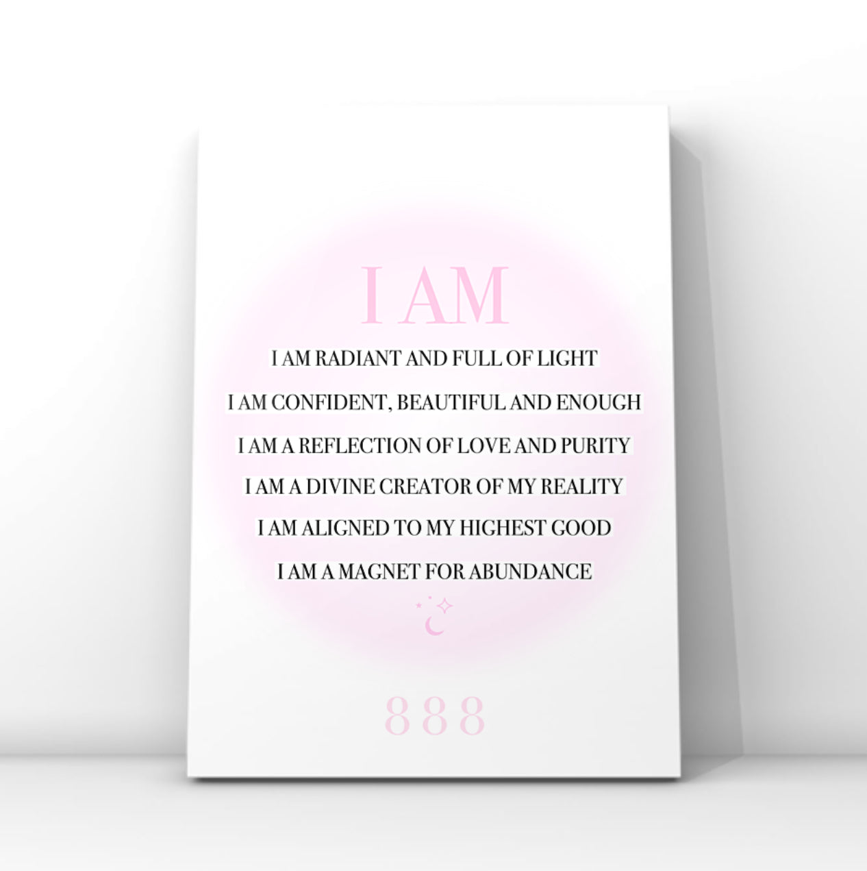 A vertical white art print with a pink circular glow and black text reading 'I AM' followed by affirmational phrases, plus '888' near the bottom, shown leaning against a light gray wall.