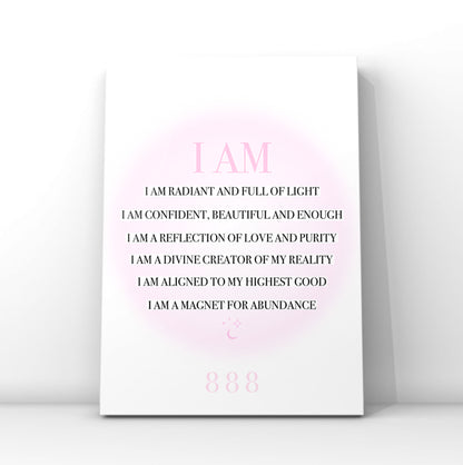 A vertical white art print with a pink circular glow and black text reading 'I AM' followed by affirmational phrases, plus '888' near the bottom, shown leaning against a light gray wall.