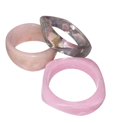 Still-life view of a three-piece acrylic candy bangle stack featuring a marbled beige bangle, a translucent iridescent oil-slick bangle, and a smooth candy pink bangle by Gypsy Soul Doll.