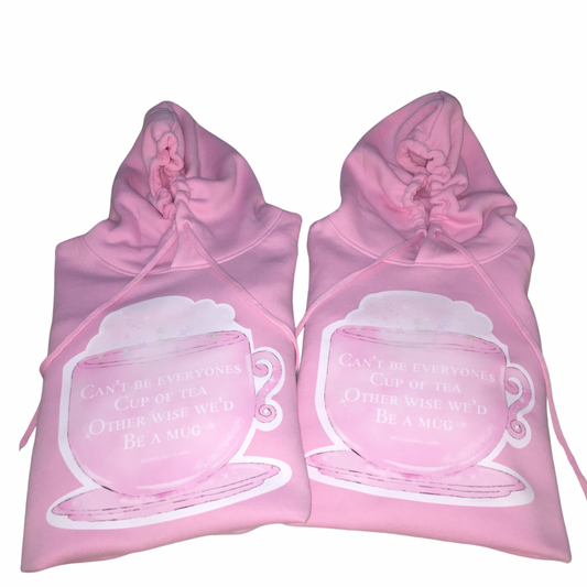 Flat lay view of two folded pink cotton oversized hoodies showcasing the matching front 'Can't Be Everyone's Cup Of Tea' graphic art prints.