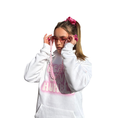 Front view of a model in a white graphic hoodie adjusting pink fashionglasses, showcasing a high-vibe festival outfit.