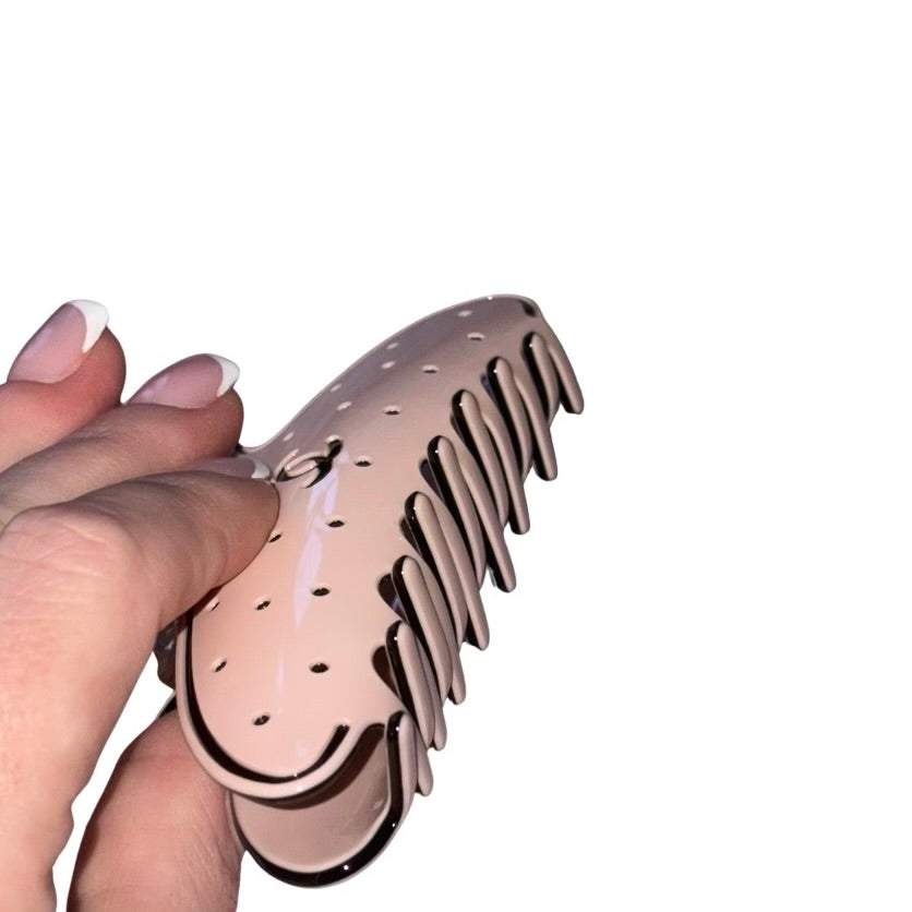 A hand holding a glossy, pink Chanel claw hair clip against a solid white background.