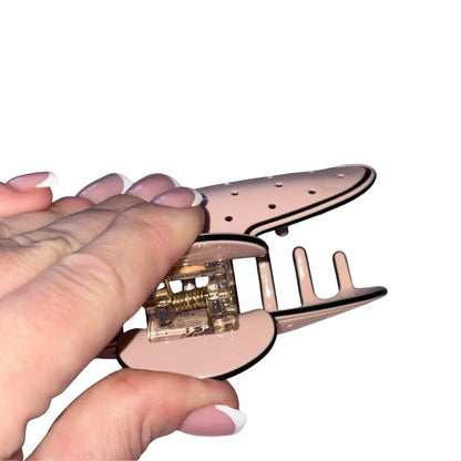 A close-up of a hand holding a rose gold Chanel claw hair clip with a clear plastic spring mechanism, set against a plain white background.