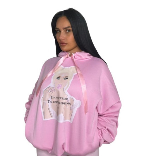 Front view of a model with long dark hair styling a roomy pink one-size hoodie featuring scrunched sleeves and a front 'I'm Not Weird, I'm Limited Edition' lollipop girl graphic.
