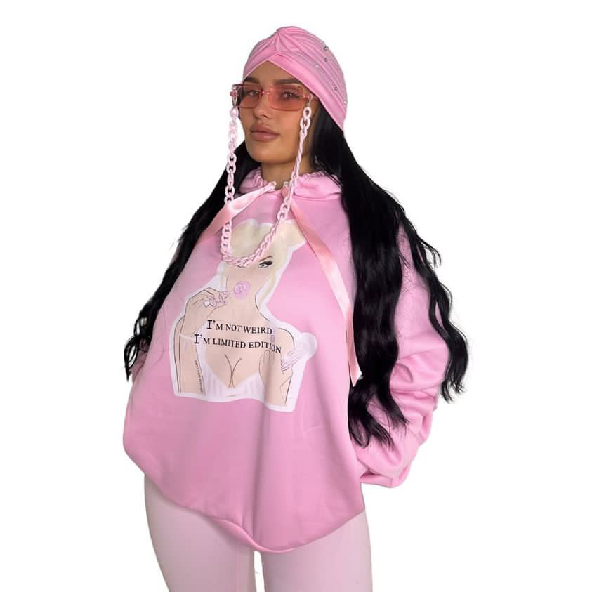Front three-quarter view of a model styling a pink scrunched sleeve hoodie with a pink boho head wrap, pink fashion glasses, and light pink leggings.