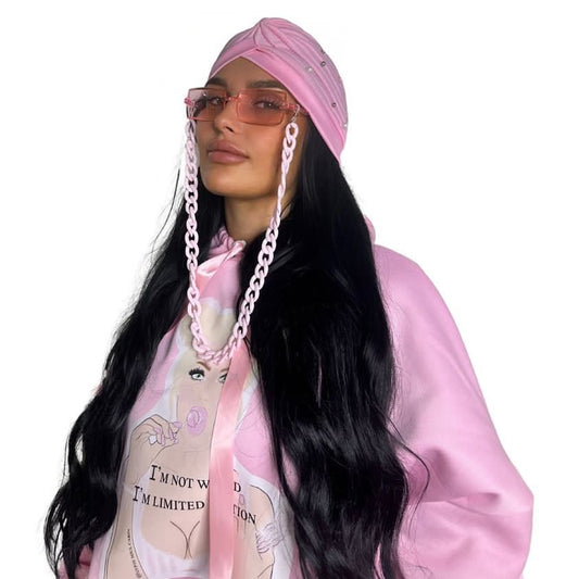 Close-up front view of a model in a pink scrunched sleeve hoodie styled with a matching pink boho Ibiza head wrap and pink fashion glasses attached to a powder pink link chain.