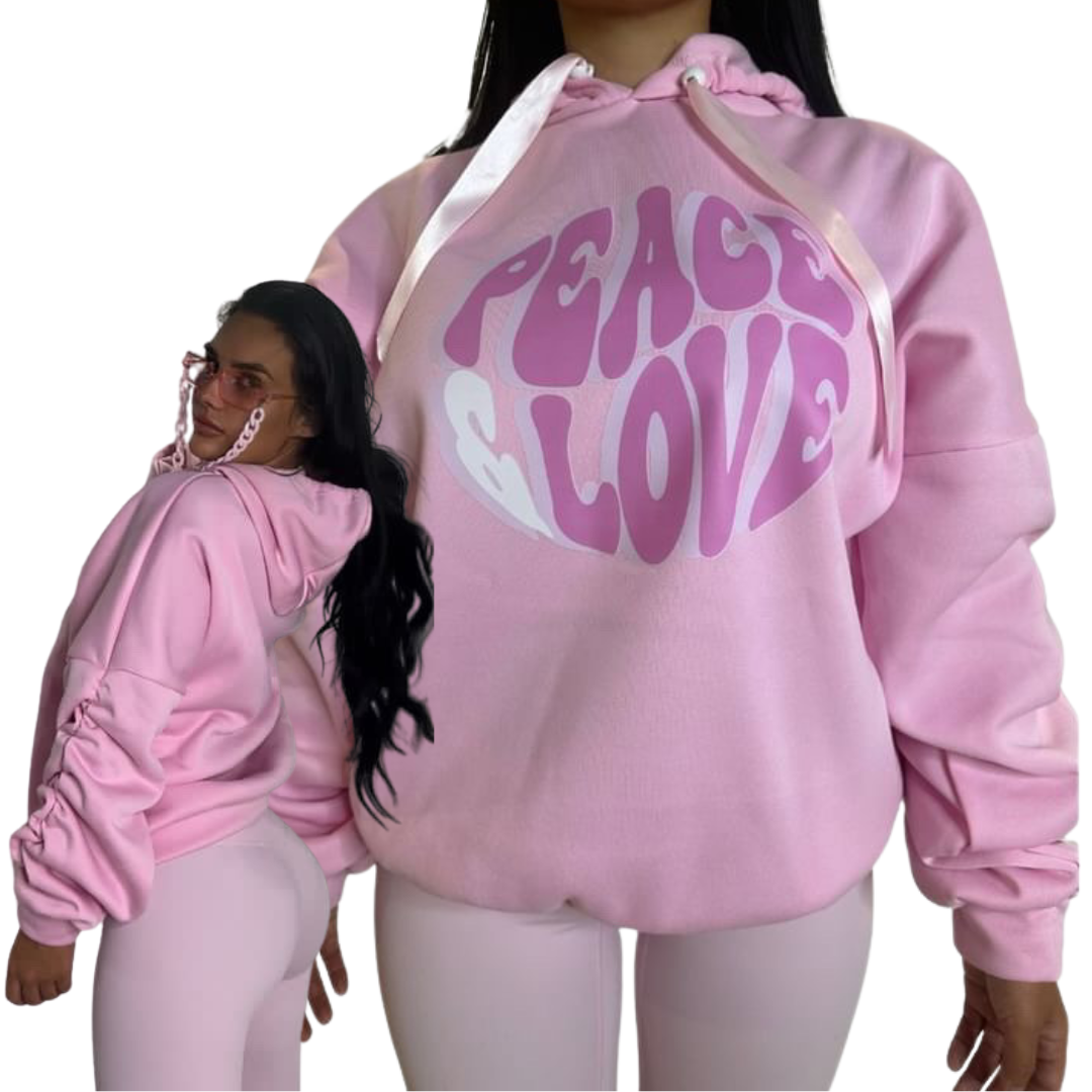 Split layout view showing the side profile and front angle of a model styling a roomy pink one-size hoodie with scrunched sleeves and a pink Peace Love bubble font graphic.