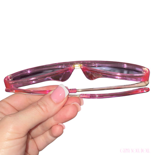 Pink translucent tortoise-style eyeglass frames held by a hand with a pink French-tipping manicure, against a solid white background.
