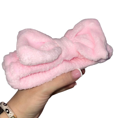 A fluffy light pink bow headband is being held by a woman's hand against a plain white background.