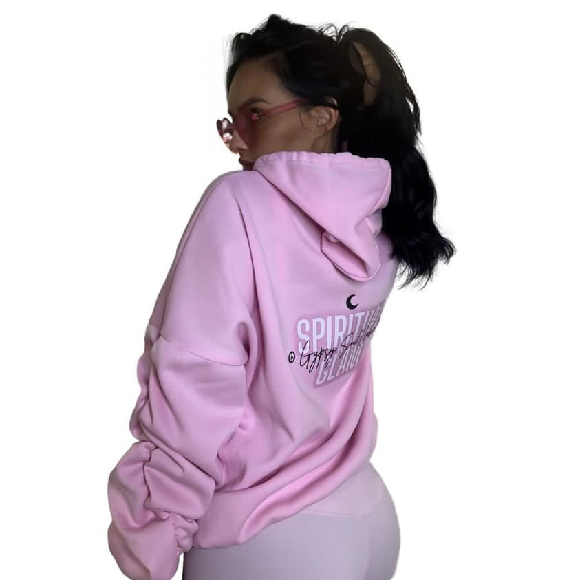 A female model wearing a light pink oversized hoodie with a graphic print on the back, shown from behind against a plain white background.