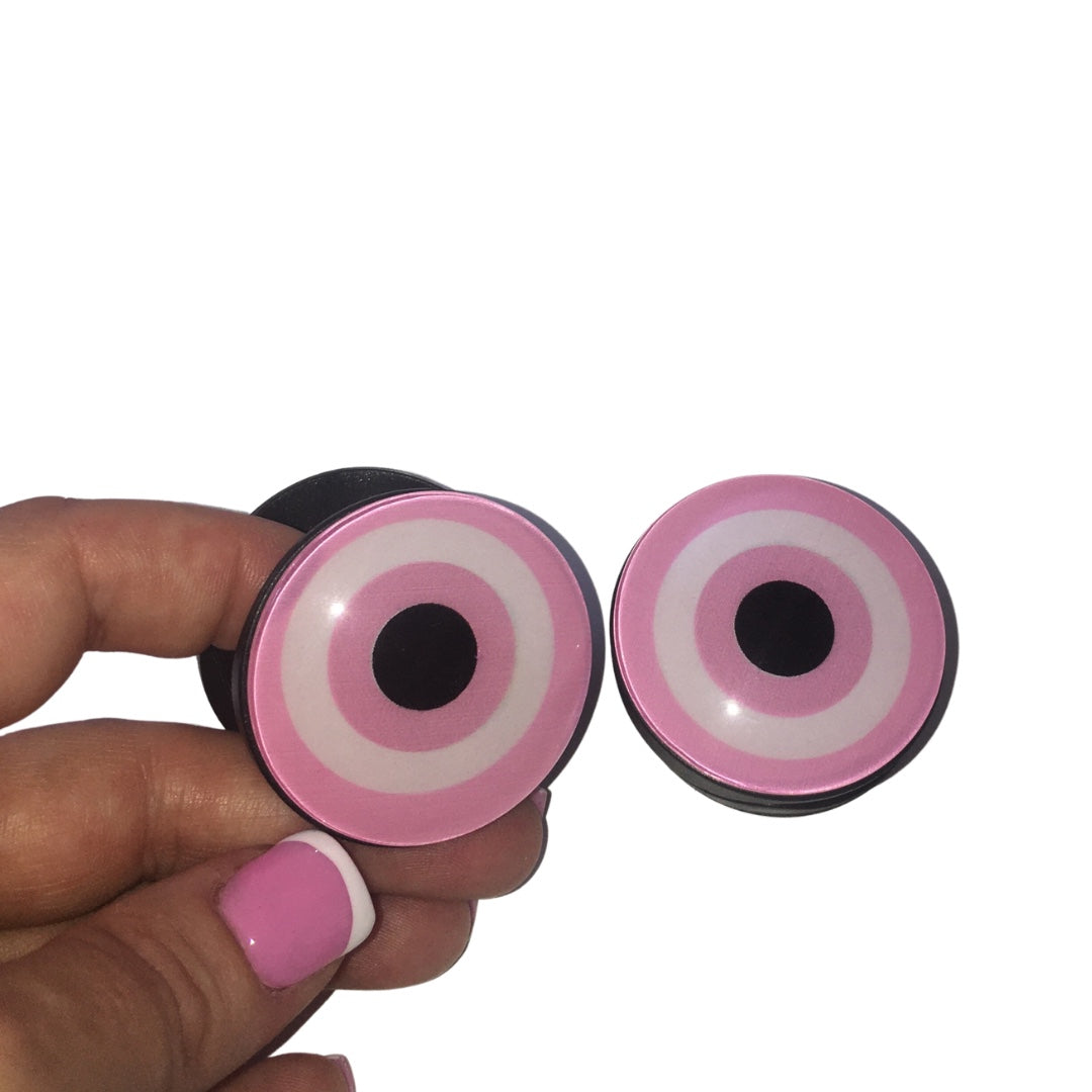 A close-up of a hand with pink French tip nails holding an expandable pastel pink and white glass-effect evil eye phone grip accessory.