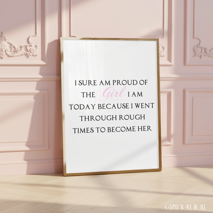Gold-framed typography print leaning on light wood flooring against a light pink panelled wall, reading I sure am proud of the girl I am today because I went through rough times to become her.
