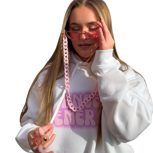 A woman with long blonde hair wearing a white hoodie with a purple gradient 'ANGEL ENERGY' graphic and a chunky pink chain fashion glasses lanyard, posing against a solid white background.