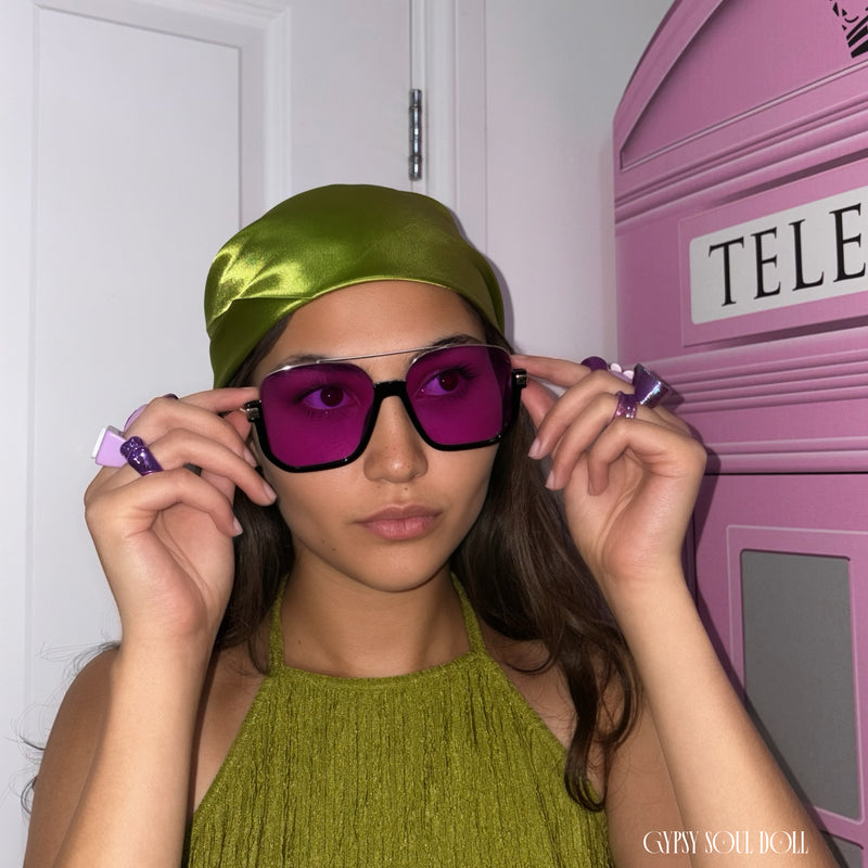 A young model wearing a pair of purple and gold fashion sunglasses with matching chunky retro rings and a boho head scarf by Gypsy Soul Doll.