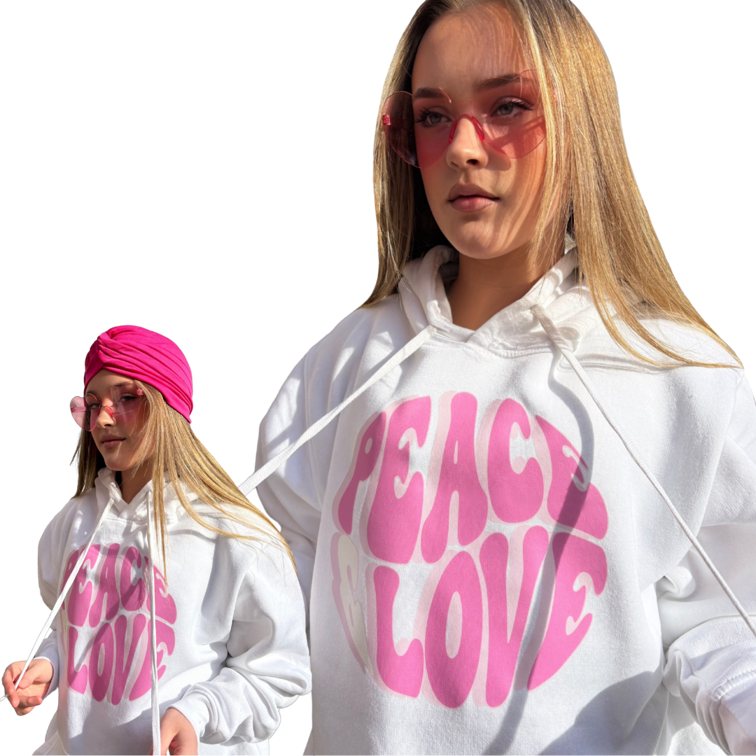 Model collage showcasing a roomy white pullover hoodie with a vibrant pink, wavy Peace & Love bubble-text graphic on the front, styled with pink fashion glasses and a pink bohemian head wrap.