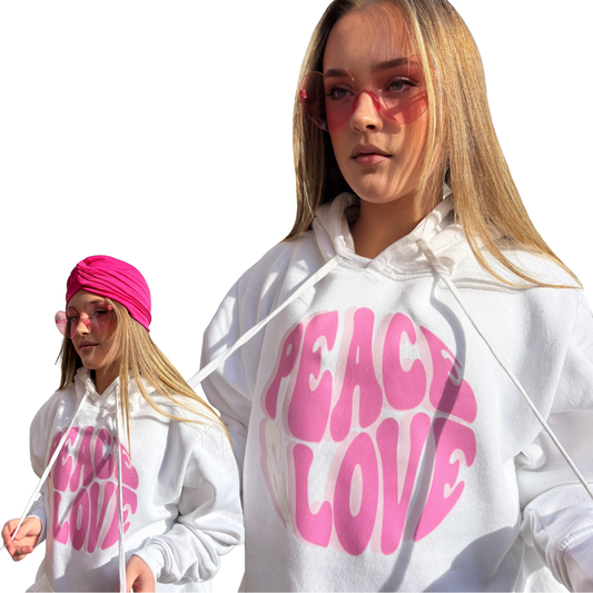 Model collage showcasing a roomy white pullover hoodie with a vibrant pink, wavy Peace & Love bubble-text graphic on the front, styled with pink fashion glasses and a pink bohemian head wrap.