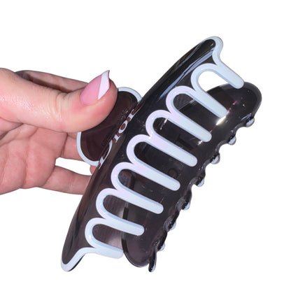 Close-up of a hand with a pink French manicure holding a high-gloss black and white designer text claw clip hair accessory.