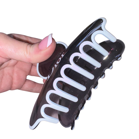 Close-up of a hand with a pink French manicure holding a high-gloss black and white designer text claw clip hair accessory.