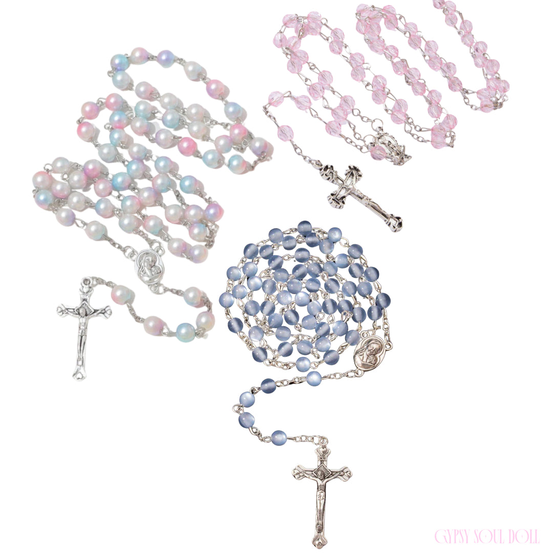 Studio product group shot featuring a trio of Gypsy Soul Doll spiritual protection rosary beads: the Aura Glow iridescent pastel pink and blue pearl style, the Ocean Breeze periwinkle blue cat-eye version, and the Sweetheart faceted transparent crystal pink variant, all displayed with their matching silver crucifix pendants on a plain white background.