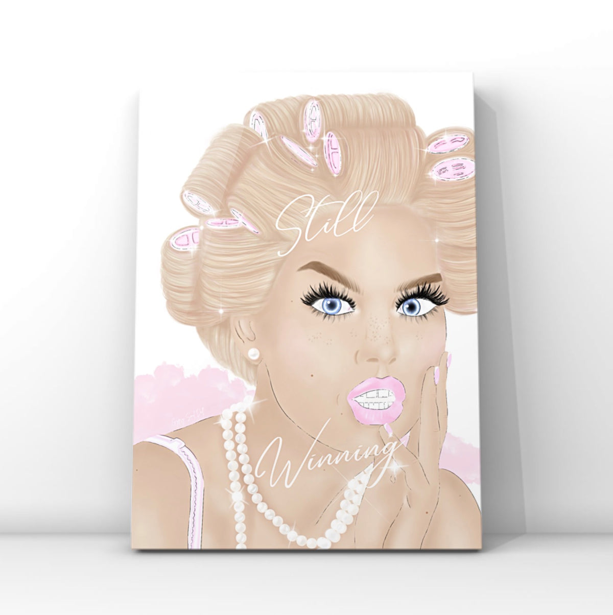 A vertical wall art print featuring a stylised illustration of a glam woman with blonde hair in pink curlers, and long lashes, wearing a pearl necklace and looking directly forward. The words 'Still Winning' are written in white script across the portrait by Gypsy Soul Doll.