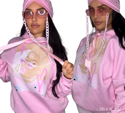 A dual-pose studio mockup of a model with long dark hair showcasing the Gypsy Soul Doll pink graphic street-style hoodie, paired with matching pink rectangle fashion glasses, a chunky pink acrylic chain strap, and a pastel pink turban style head wrap embedded with white pearls