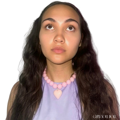 Model showcasing the Gypsy Soul Doll pink chunky bubblegum bead necklace with a large matching pastel pink puffy heart pendant worn with a lilac top.