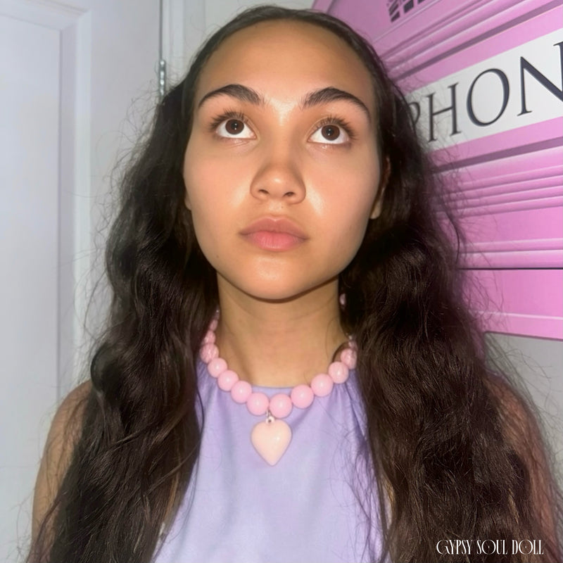 Model showcasing the Gypsy Soul Doll pink chunky bubblegum bead necklace with a large matching pastel pink puffy heart pendant, standing next to a trendy pink telephone box backdrop.