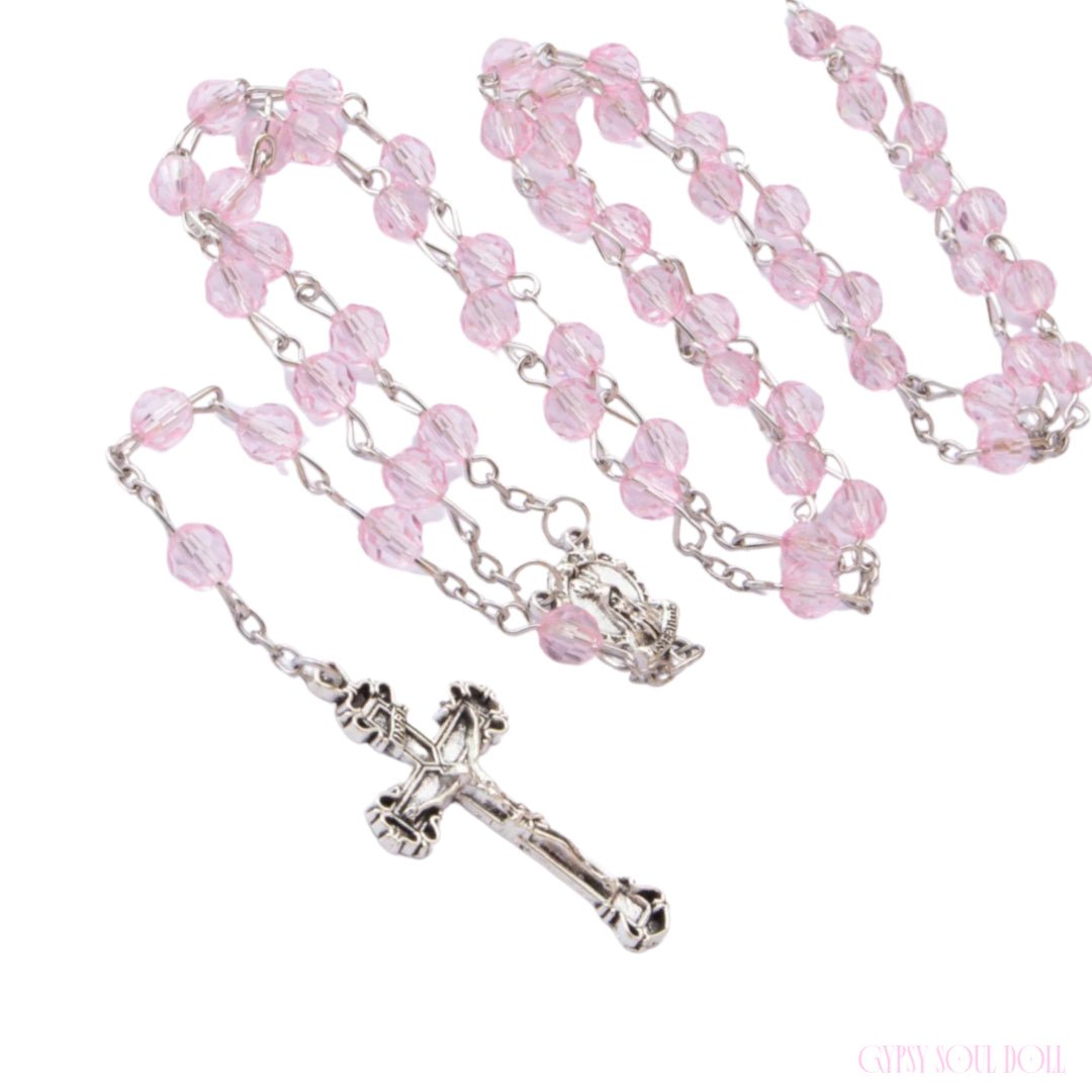 A rosary necklace featuring light pink faceted glass beads on a silver-tone metal chain, with a detailed silver crucifix and centerpiece, displayed on a clean white background.