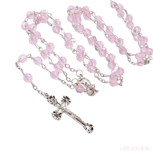 A rosary necklace featuring light pink faceted glass beads on a silver-tone metal chain, with a detailed silver crucifix and centerpiece, displayed on a clean white background.
